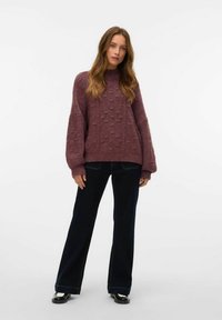 Un pull surdimensionné en mauve foncé, avec un motif texturé, des manches larges et des bordures côtelées, associé à un jean droit foncé et des chaussures noires.