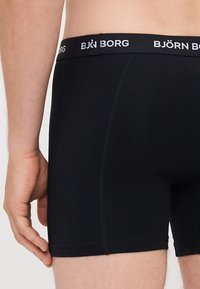 Black boxer briefs made of smooth fabric, featuring a wide waistband with the "BJÖRN BORG" logo. Designed for a snug fit with a mid-thigh length.