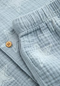 Tissu texturé bleu clair avec motif étoile matelassé, montrant une taille élastique et un détail de bouton en bois sur un vêtement doux.