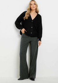 Cardigan noir en tricot avec un décolleté en V profond, de grands boutons et des manches volumineuses, associé à un pantalon gris large taille haute.