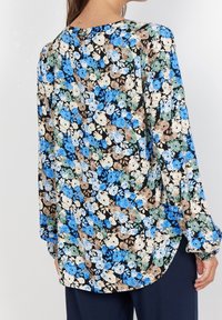 Blommig blus med svart bakgrund, prydd med blå, krämiga och gröna blommor. Långa ärmar, rundad fåll och lätt tygstruktur.