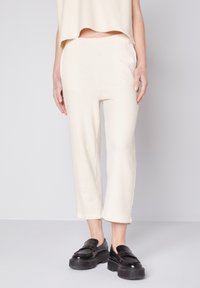 Cremefarvede, teksturerede loungebukser med elastisk talje, beskåret længde, parret med sorte platform loafers. Simpelt design og afslappet pasform.