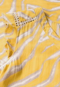 Un indumento giallo con un motivo a onde grigie. Il tessuto presenta una texture liscia con un bordo decorativo sulla spalla.