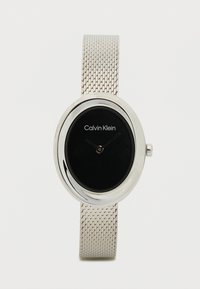 Ρολόι με μεταλλική αλυσίδα σε ασημένιο τόνο και οβάλ μαύρο καντράν, με μινιμαλιστικά δείκτες ωρών και λεπτών, που φέρει το λογότυπο "Calvin Klein".