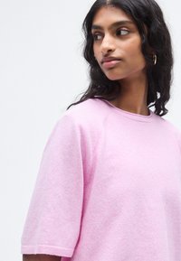 Pull rose à manches courtes avec une texture douce et un col rond. Présente une coupe décontractée et des détails de couture minimalistes.