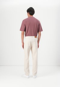 Camiseta de manga corta color burdeos combinada con pantalones de color crema. Los pantalones tienen un acabado texturizado y una etiqueta de cuero en la parte trasera.