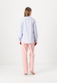 Camicia a maniche lunghe a righe bianco e azzurro chiaro con colletto arruffato, abbinata a pantaloni a vita alta rosa chiaro. Visibili dettagli della trama chiara.