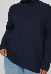 Golfino a collo alto navy realizzato in tessuto testurizzato, con maniche lunghe e vestibilità rilassata. Abbinato a jeans denim azzurri.