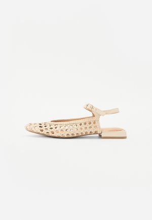 Scarpe piatte intrecciate beige con lati aperti, punta arrotondata e cinturino alla caviglia con fibbia. Tacco quadrato basso e suola liscia.
