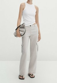 Lichtgrijze cargopantalons met zijzakken, gecombineerd met een witte mouwloze top. Zwarte sandalen en een grijze clutch tas maken de outfit compleet.