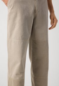Light beige trousers in a soft, textured fabric with a wide leg design. Features stitching details and visible seams, enhancing durability.