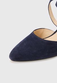 Mørkeblå suede spiss tå sko med sideløsning og ankelrem. Glatt tekstur med flat såle. Enkel sømdetalj.