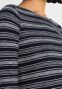 Haut rayé bleu marine et blanc avec un col rond et une silhouette ajustée, fabriqué à partir d'un tissu doux et extensible au toucher lisse.