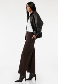 Cazadora bomber de cuero negro, camiseta blanca y jeans anchos marrones con dobladillo deshilachado, combinados con botas de tacón alto negras con punta.