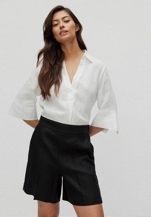 White linen shirt with a v-neck and wide sleeves, paired with black linen shorts featuring side pockets and a structured waist.