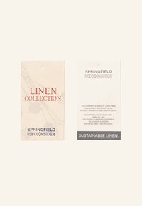 Deux étiquettes en tissu sur un fond clair. Une étiquette présente une couleur beige avec du texte rouge et bleu ; l'autre est blanche avec du texte gris, mettant en avant du lin durable.