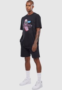 Sort bomulds T-shirt med et grafisk motiv af en pink flip-telefon og ordet "Hotline." Sammen med sorte shorts og hvide sneakers og sokker.