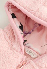Veste en fausse fourrure rose avec une doublure intérieure à motifs de rose et des bords rose clair. Elle dispose d'une fermeture éclair lisse avec des accents métalliques.