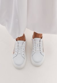 Sneaker bianchi con tomaia in pelle liscia, design con lacci, dettagli testurizzati in un colore chiaro e punta arrotondata.