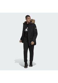 Černá parka s přírodní kožešinou na kapuci, dva přední kapsy a knoflíkové zapínání. Nosit přes černou mikinu a odpovídající kalhoty.