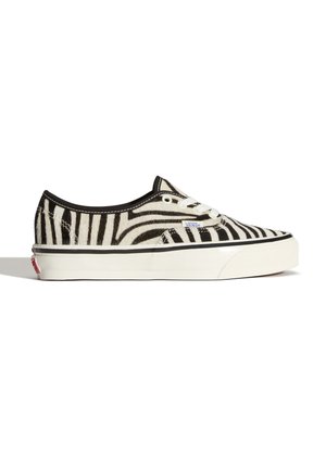 Zapatilla Vans de caña baja con rayas de cebra en blanco y negro, cordones blancos y suela blanca gruesa con ribete negro y etiqueta con el logo de Vans.