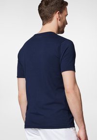 Granatowa koszulka z krótkim rękawem wykonana z materiału przypominającego bawełnę; ma okrągły dekolt i jest dopasowana w okolicy ramion oraz rękawów.