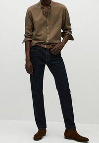 Bruine button-up shirt met een zak, donkerblauwe rechte spijkerbroek enbruine enkellaarsjes. Eenvoudig, klassiek ontwerp met een getailleerde pasvorm.