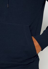 Sudadera de algodón azul marino con un bolsillo frontal, puños y cintura acanalados. Textura suave y cordón ajustable en el escote.