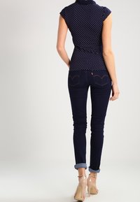 Marinblus med prickar, figursydd med korta ärmar, i kombination med mörk denim skinny jeans som är uppvikta vid anklarna, kompletterat med nude högklackade skor.