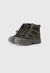 Bottes de randonnée vertes avec un design montante, en matériau imperméable, semelle en caoutchouc texturée, et accents orange sur la semelle et les lacets.