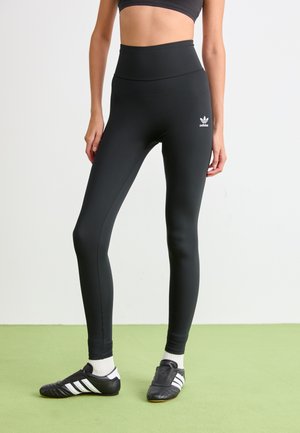 Leggings negre cu talie înaltă dintr-un material elastic, având un mic logo alb Adidas pe picior. Textură netedă, design aderent.