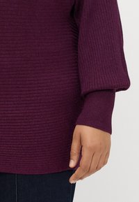Rippstrickpullover in Dunkellila mit weiten Ärmeln und lockerer Passform. Besitzt ein strukturiertes Design und ein weiches, gemütliches Aussehen.