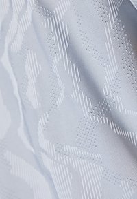 Tela texturizada en azul pálido con un patrón de formas geométricas elevadas y líneas horizontales. Acabado suave y detalle de textura tejida visible.