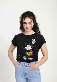 Černé bavlněné tričko s krátkým rukávem, na kterém je bílá grafika Mickey Mouse, držící duhové znamení míru, v kombinaci se světle modrými džíny.