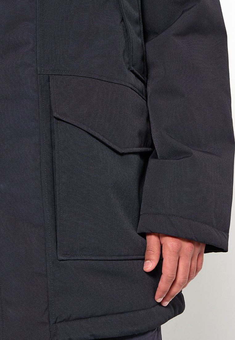 Manche de veste rembourrée bleu marine foncé en tissu texturé, avec une poche à rabat et un poignet renforcé. La couture est soignée et uniforme.