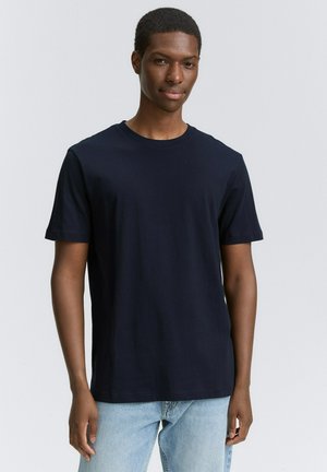 Navyblaue Baumwoll-T-Shirt mit kurzen Ärmeln, Rundhalsausschnitt und lockerer Passform, kombiniert mit hellblauen Jeans.