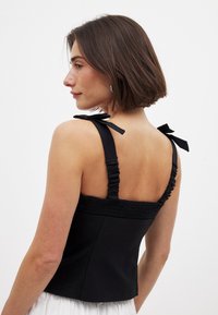 Top nero con spalline arricciate e dettagli sul retro smockati. Il design ha una silhouette aderente e una texture liscia, adatta per il layering.