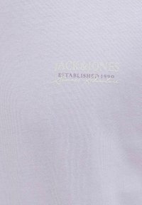 Šviesiai pilka trumpomis rankovėmis marškinėliai pagaminti iš minkštos medvilnės. Su baltu logotipu, kuriame yra "JACK & JONES" ir "Įkurta 1990" subtiliu siuvinėjimu.