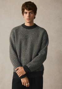 Grau und schwarz gestreifter Pullover mit Rundhalsausschnitt und gerippten Bündchen, aus strukturiertem Strickmaterial gefertigt.