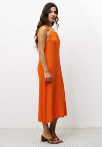 Oranges ärmelloses Kleid aus strukturiertem Stoff, knöchellang, mit seitlichen Schlitzen und gebundenen Schulterträgern, kombiniert mit braunen Sandalen mit gestapeltem Absatz.