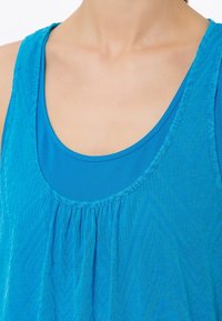 Blå linne med ett lagerdesign som har ett texturerat yttertyg och ett slätt innerlager. Rundad halsringning med plisserade detaljer.