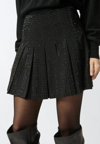 Gonna nera plissettata con motivi testurizzati e piccoli accenti lucenti, con vita aderente e lunghezza moderata.