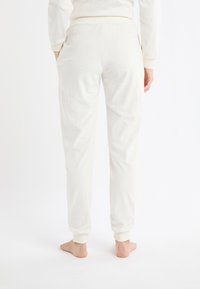 Białe spodnie dresowe z wzorem gwiazd, wykonane z miękkiego materiału, z prążkowanym paskiem w talii i ściągaczami, wyposażone w boczne kieszenie.