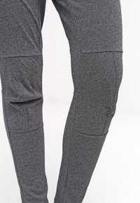 Gros plan sur un pantalon en tissu gris texturé avec des détails de couture et des renforts au niveau des genoux.
