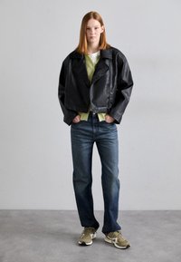 Svart cropped skinnjakke med krage, kombinert med en lys grønn topp, blå jeans og beige sneakers. Glatt tekstur og avslappet passform.