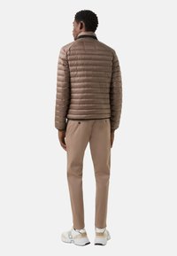 Bruine pufferjas met een doorgestikt ontwerp, gecombineerd met lichtbruine broek en witte sneakers met beige accenten en een gestructureerde zool.