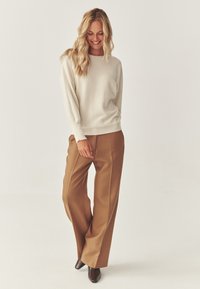 Lys beige sweater med en afslappet pasform, parret med høj talje, brede brune bukser og brune spidse ankelstøvler.