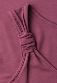 Gros plan d'un vêtement en tissu rose poussiéreux avec un détail de nœud froncé le long d'une couture courbée.