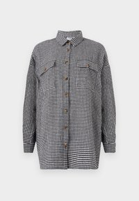 Košile s dlouhými rukávy v černobílém houndstooth vzoru, s knoflíkovým zapínáním vpředu a dvěma kapsami na hrudi. Obsahuje standardní límec a hnědé knoflíky.
