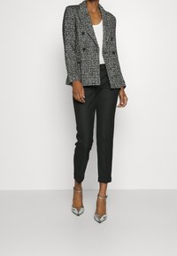 Zwart-witte getextureerde double-breasted blazer met ingezette revers, gecombineerd met op maat gemaakte zwarte broek en patroonhooggehakte schoenen.